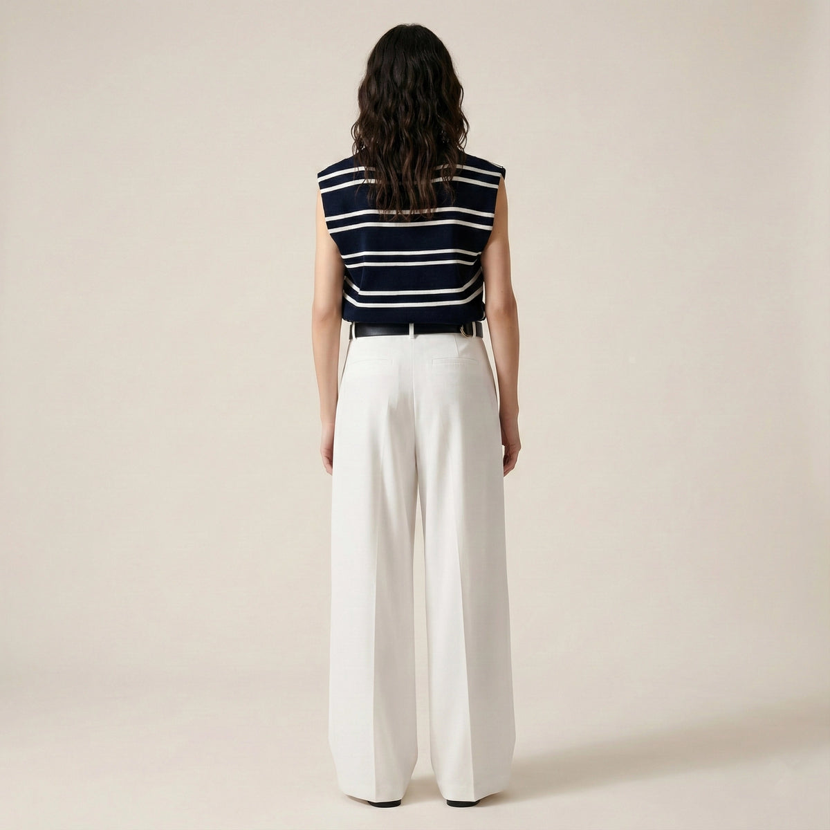 Person wearing a striped sleeveless top and white pants on a beige background