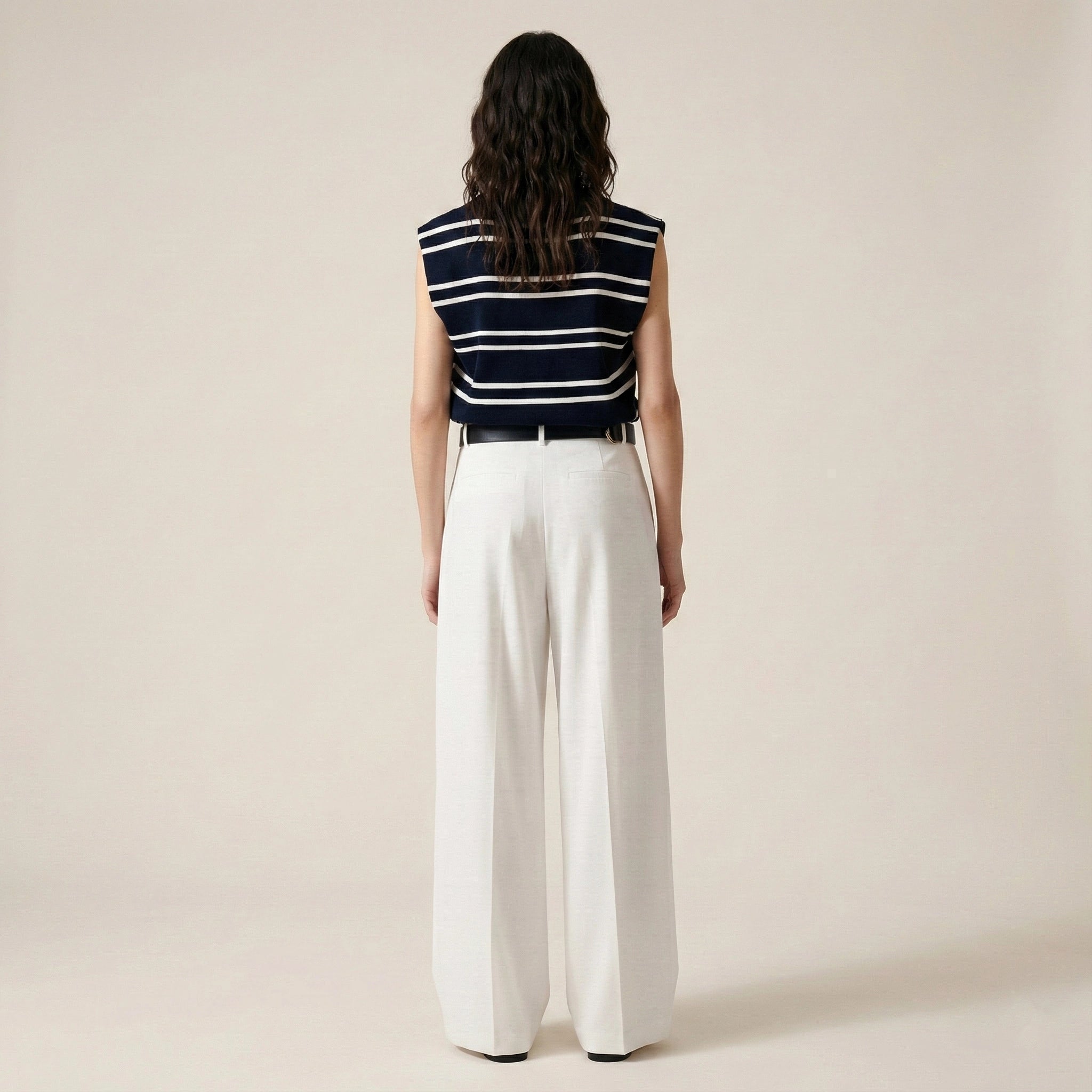 Person wearing a striped sleeveless top and white pants on a beige background