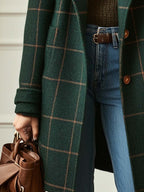 Person wearing a green plaid coat with a brown bag and blue jeans.