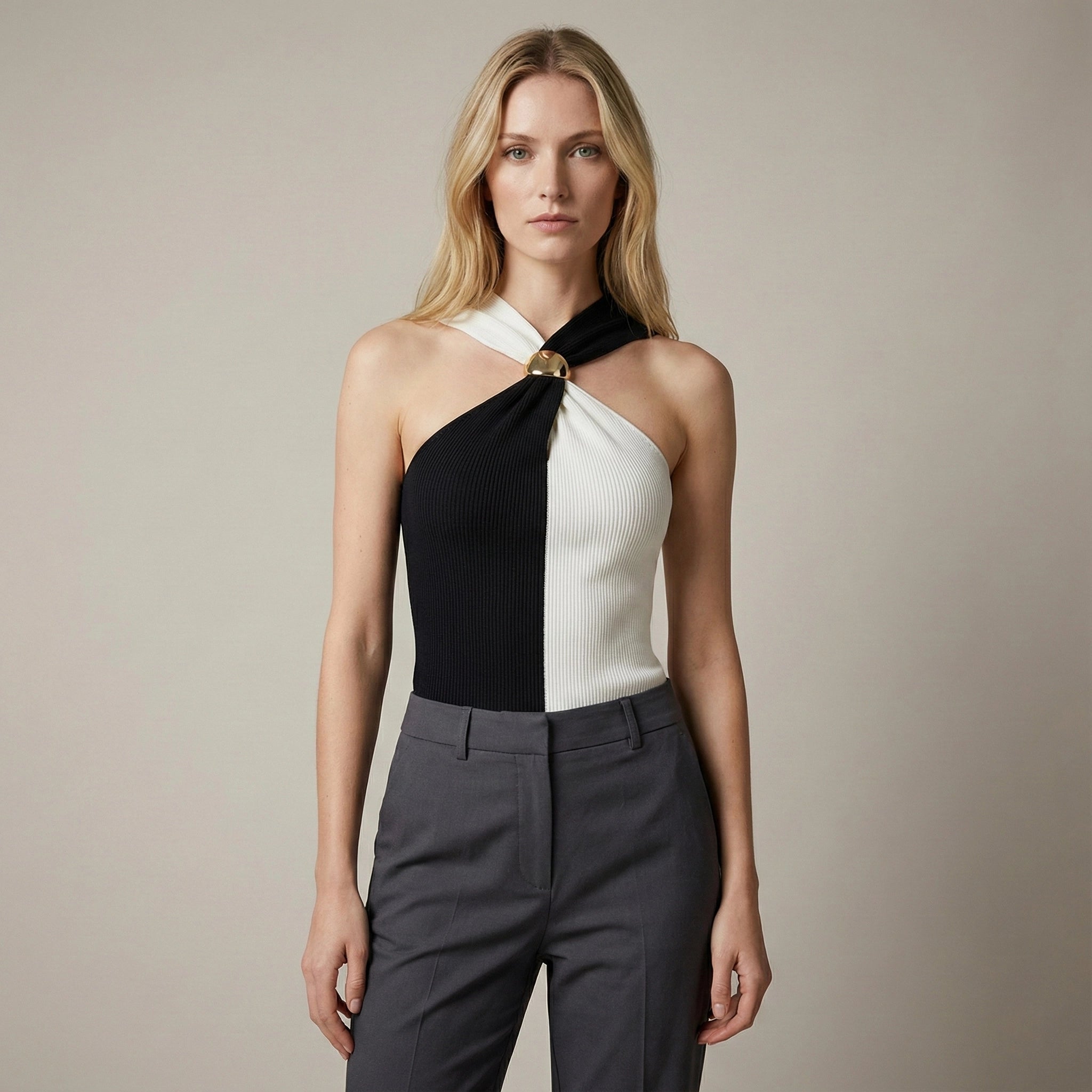 Woman wearing a black and white halter top with gray pants against a beige background