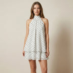 Woman wearing a white dress with black polka dots against a beige background