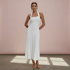 Woman wearing a white halter neck dress against a pink wall.