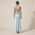 Woman wearing a light blue halter neck dress with bow details on a beige background