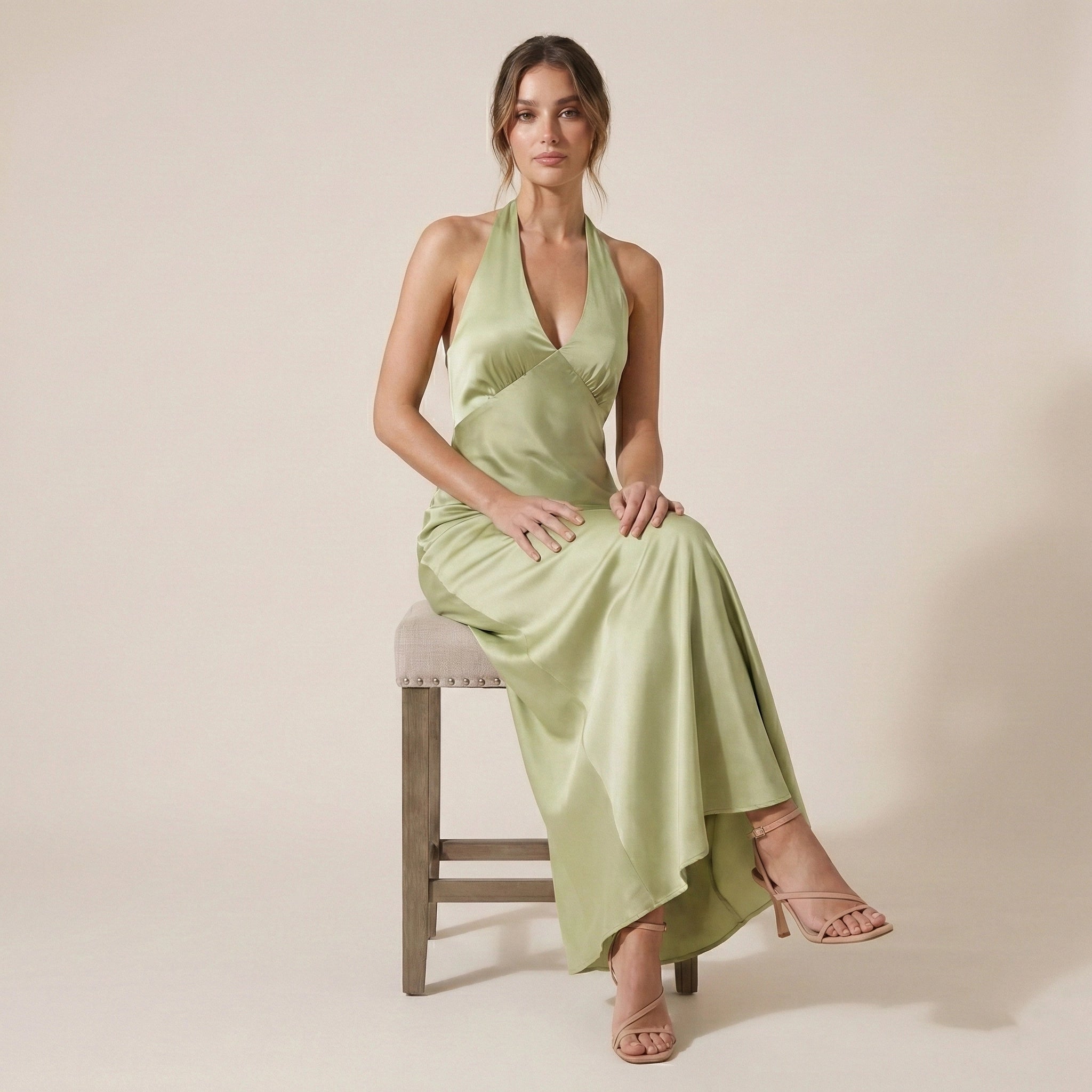 Woman in a light green dress sitting on a stool against a plain background
