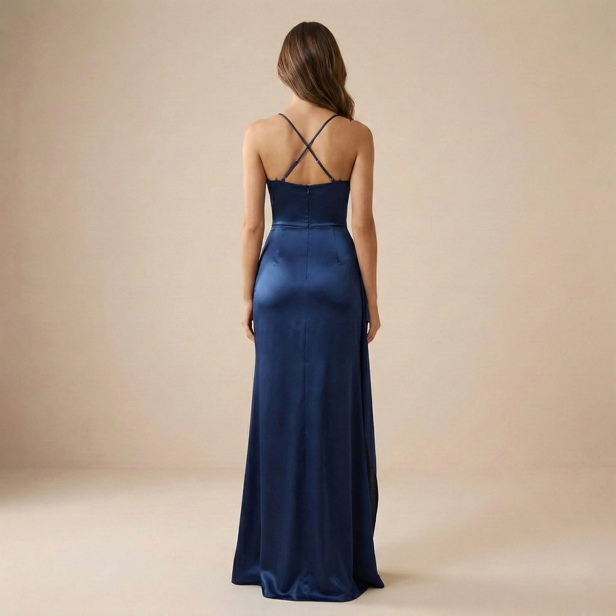 Woman wearing a long navy blue dress with thin straps on a beige background