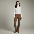 Woman wearing a white turtleneck and brown pants against a plain background