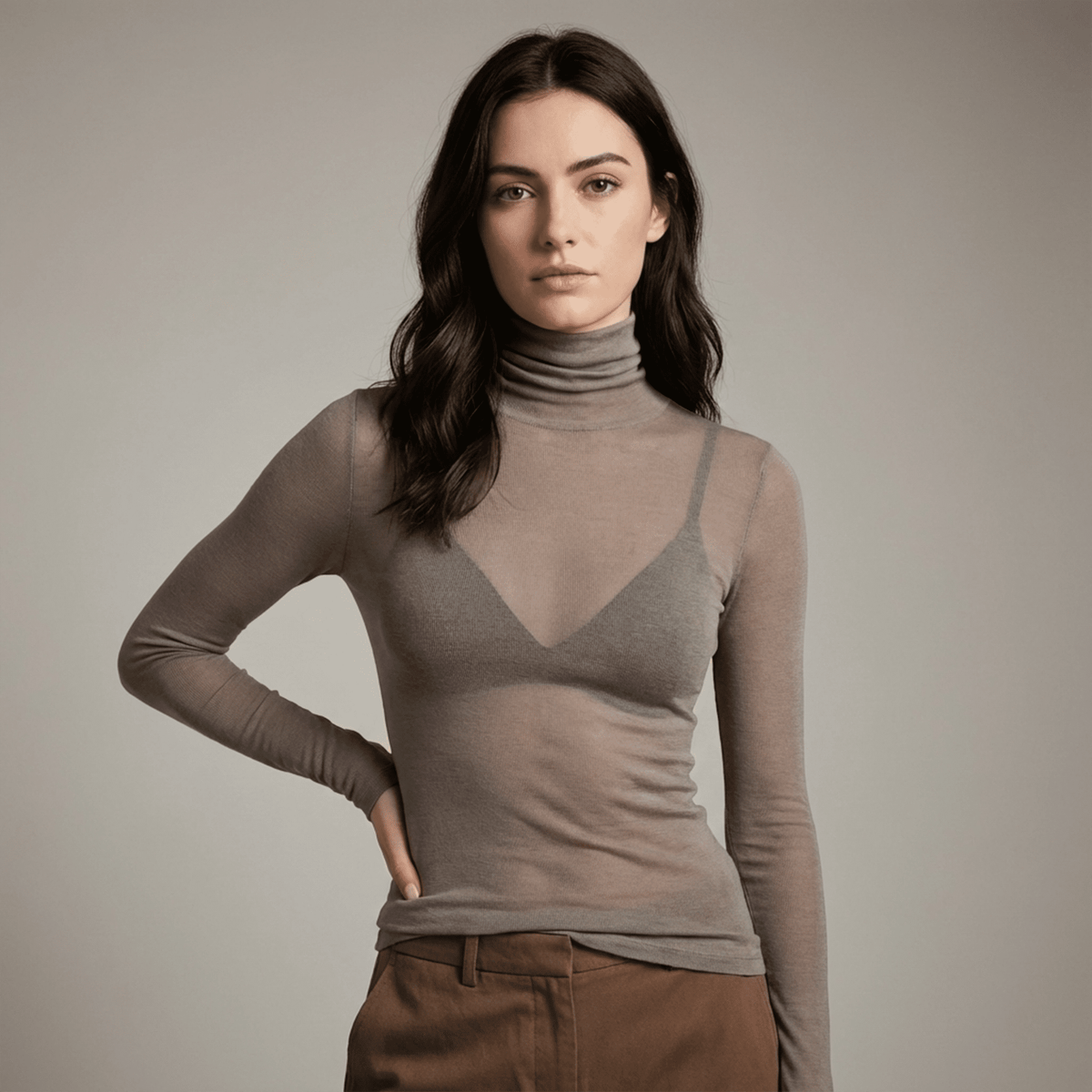 Woman wearing a brown turtleneck over a sheer top against a plain background