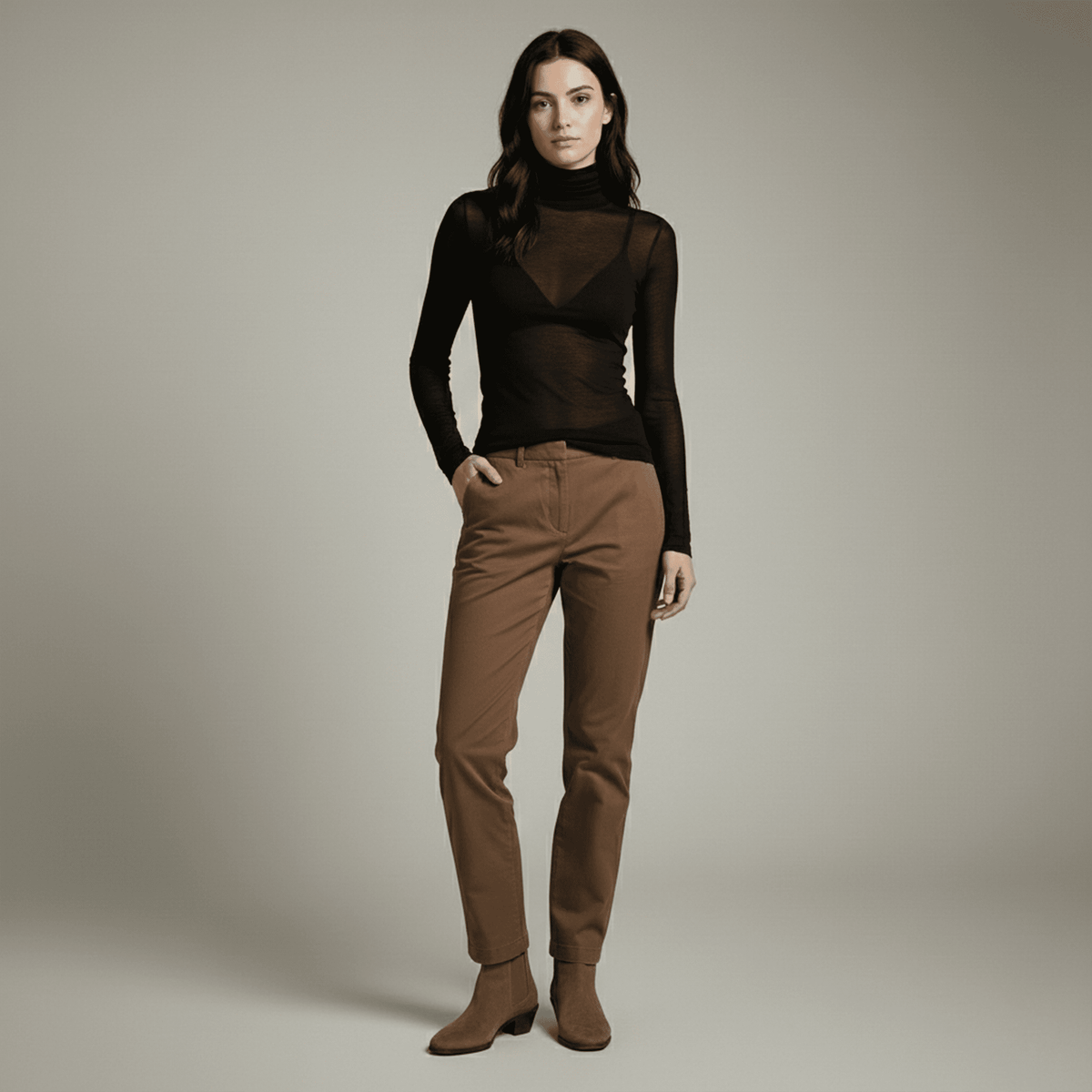 Woman wearing a black sheer top and brown pants against a neutral background