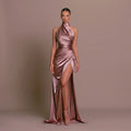 Model wearing a pink satin gown with a high slit on a brown background