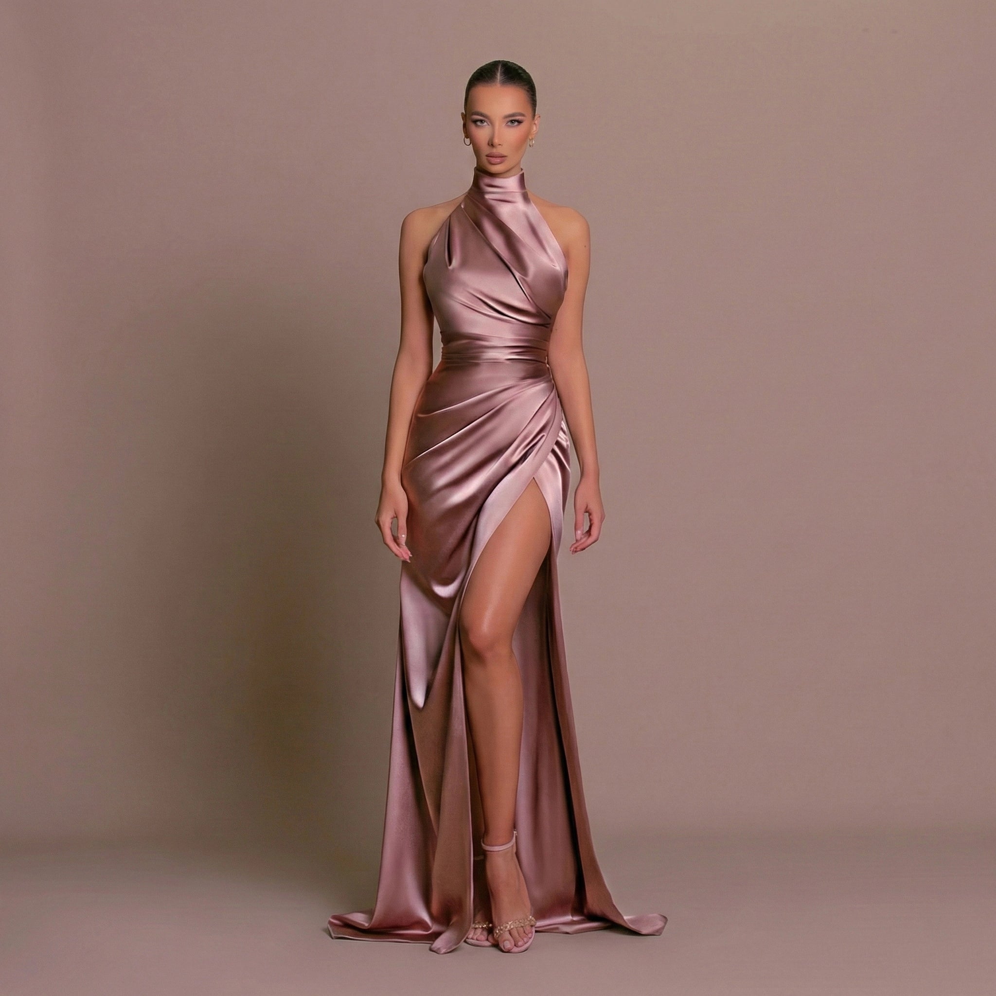 Model wearing a pink satin gown with a high slit on a brown background