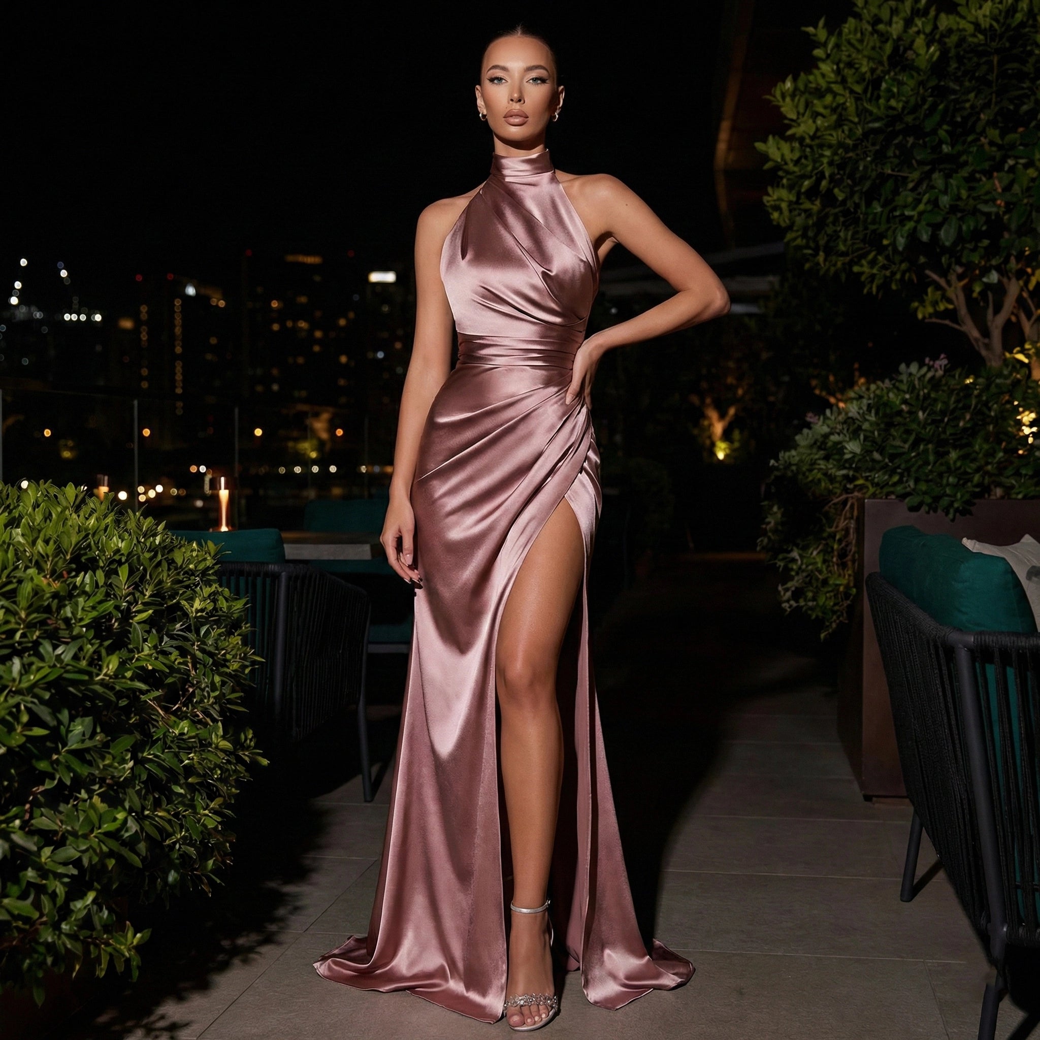 Woman in a pink satin dress standing outdoors at night with city lights in the background