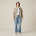 Woman wearing a beige checkered jacket, white shirt, and blue jeans on a beige background