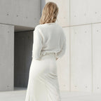 Person wearing a white outfit standing in a minimalistic setting with concrete walls.
