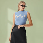 Woman wearing a light blue sleeveless top with floral designs and black pants on a white background