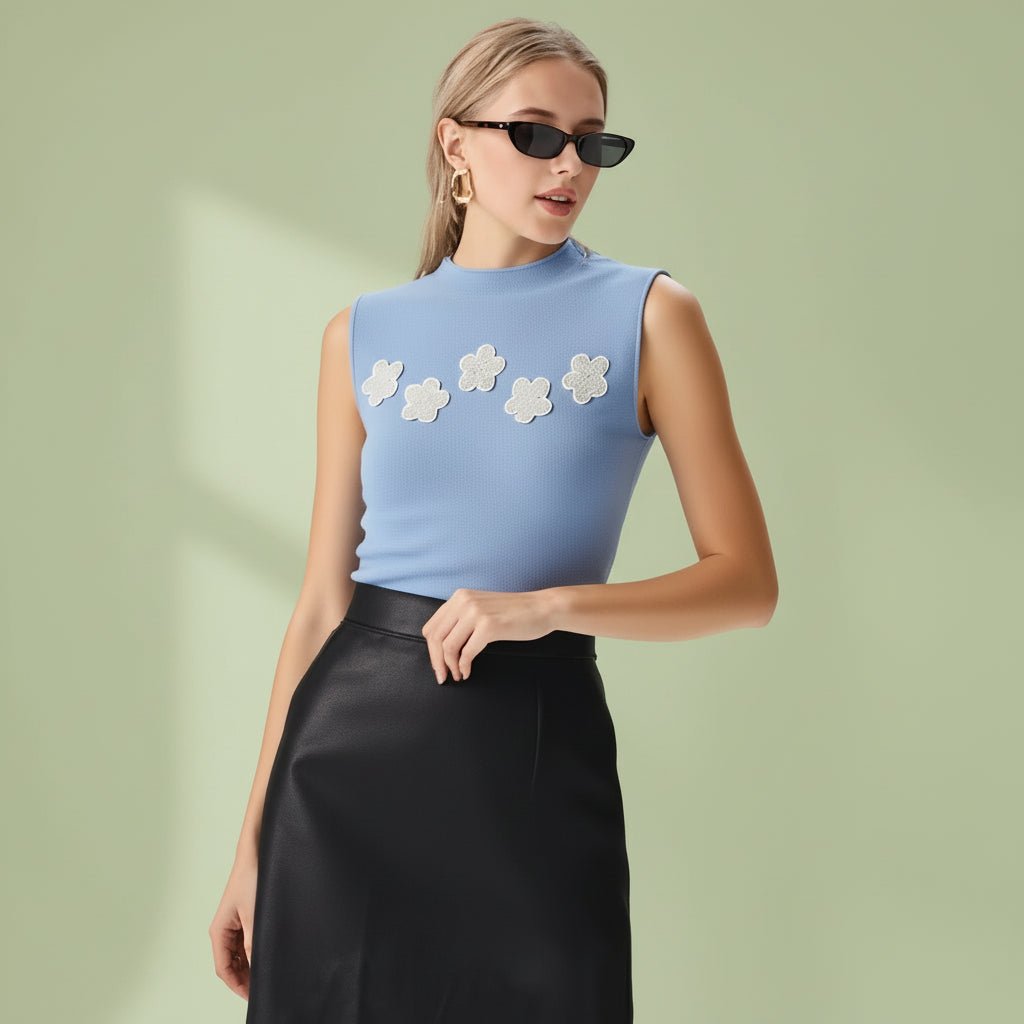 Woman wearing a light blue sleeveless top with floral designs and black pants on a white background