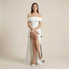 Woman wearing a white off-shoulder gown with a high slit on a plain background