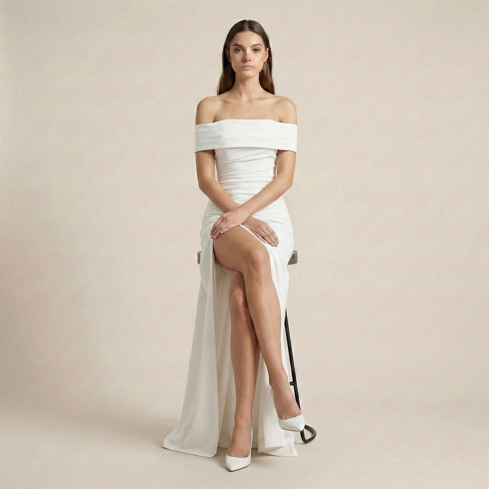 Woman wearing a white off-shoulder gown with a high slit on a plain background