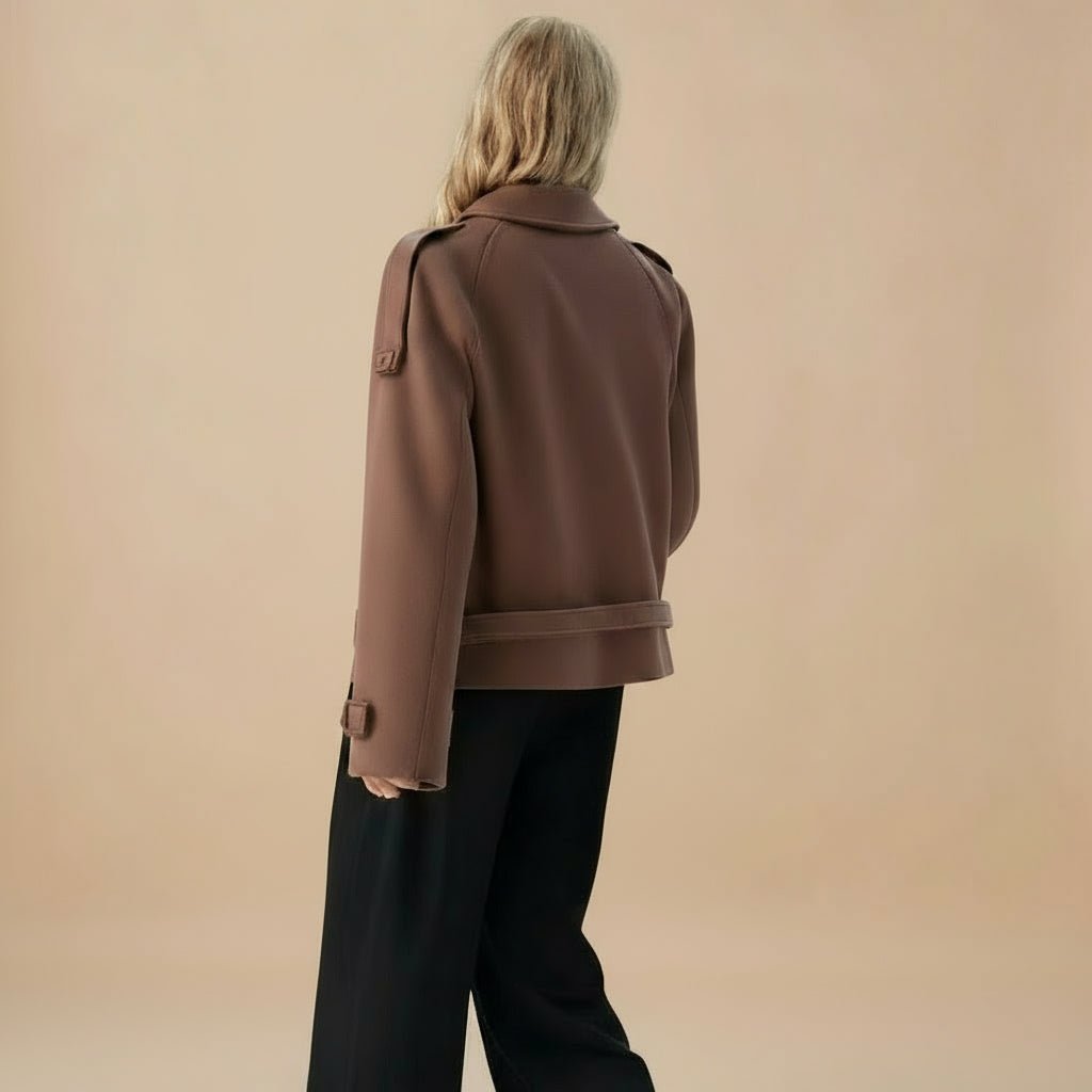 Person wearing a brown coat and black pants against a beige background