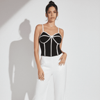 Woman wearing a black and white geometric top with white pants on a light gray background