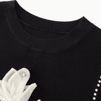 Black sweater with white floral design and pearl details on a white background