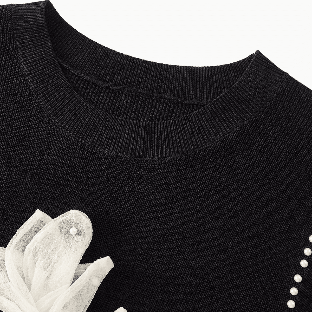 Black sweater with white floral design and pearl details on a white background
