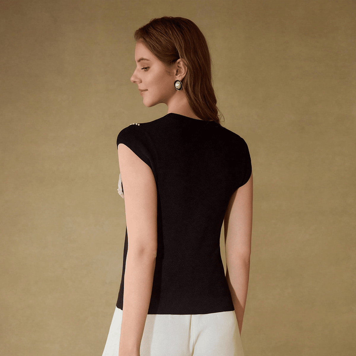 Woman wearing a black top with cut-out shoulders against a beige background