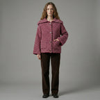 Person wearing a patterned jacket and brown pants on a gray background