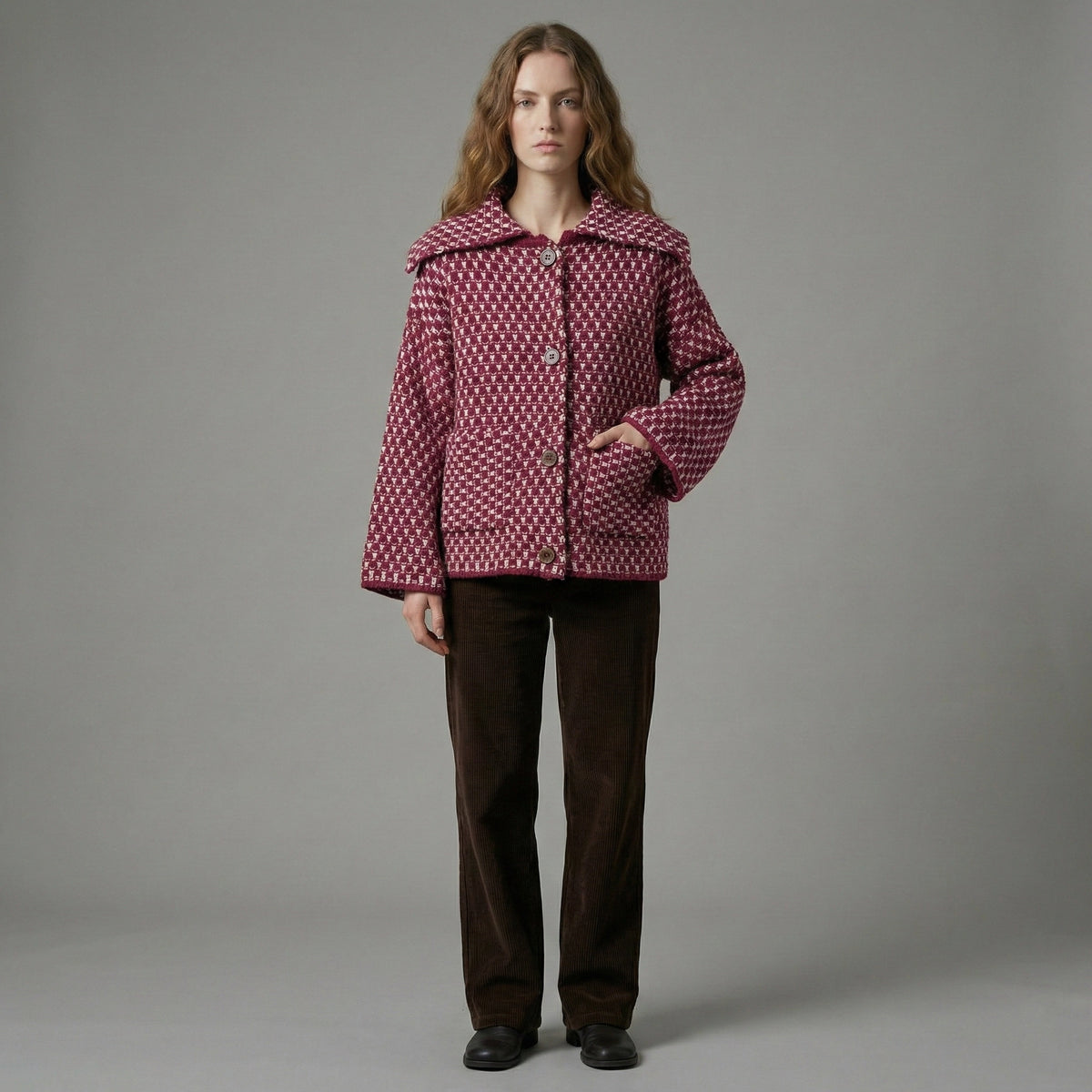 Person wearing a patterned jacket and brown pants on a gray background