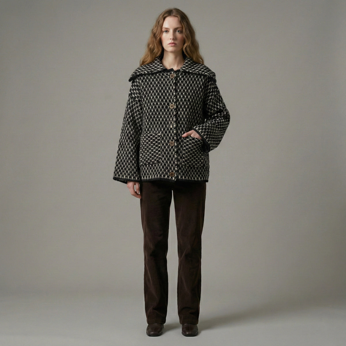 Woman wearing a patterned coat and brown pants against a plain background