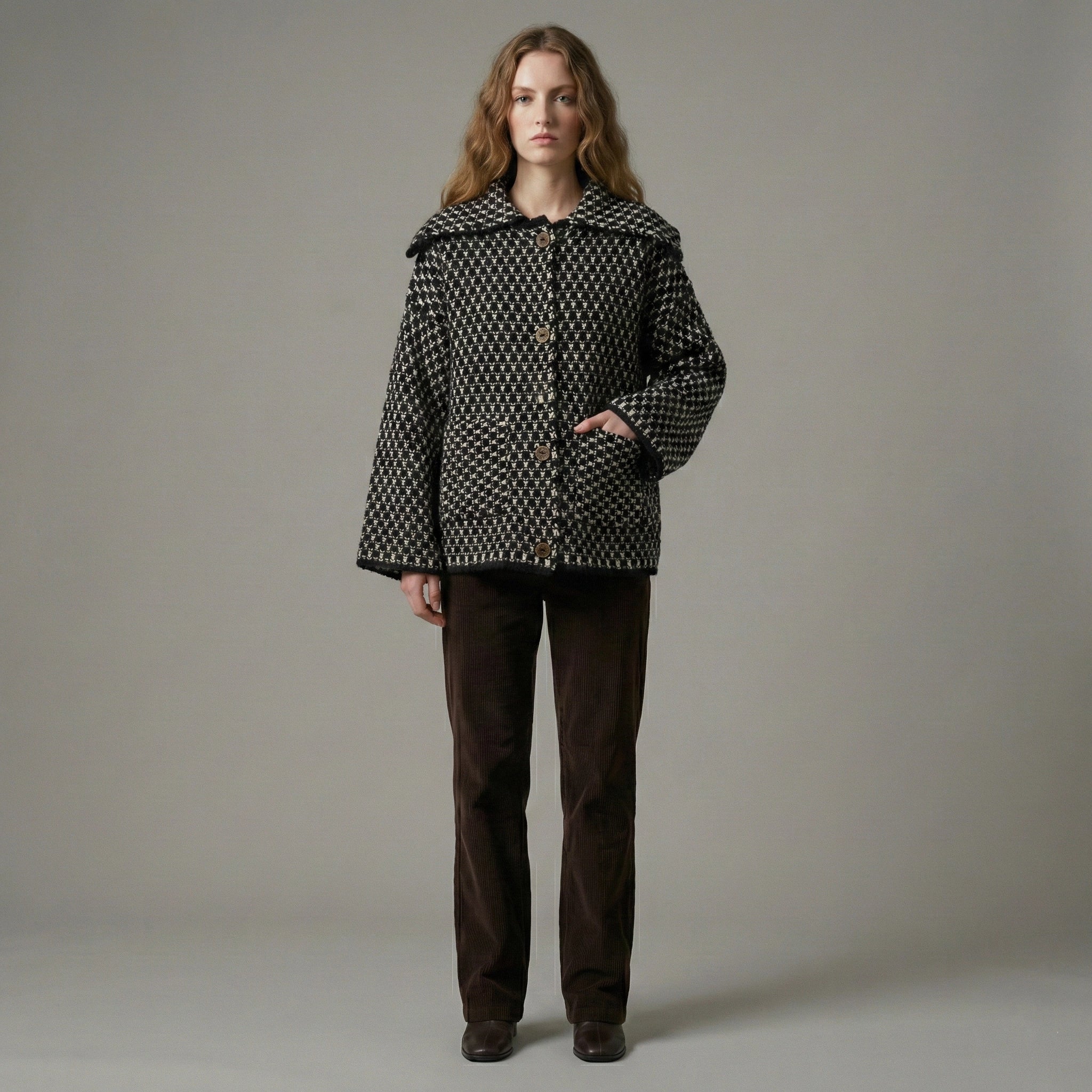 Woman wearing a patterned coat and brown pants against a plain background