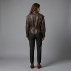 Person wearing a brown leather jacket and dark pants on a gray background