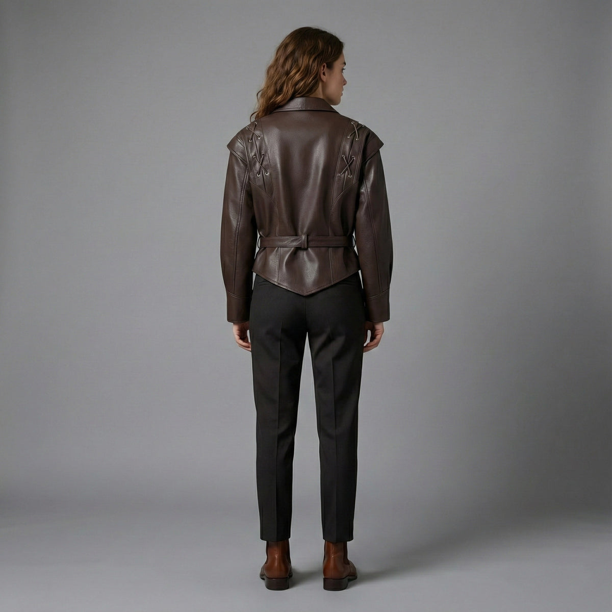 Person wearing a brown leather jacket and dark pants on a gray background