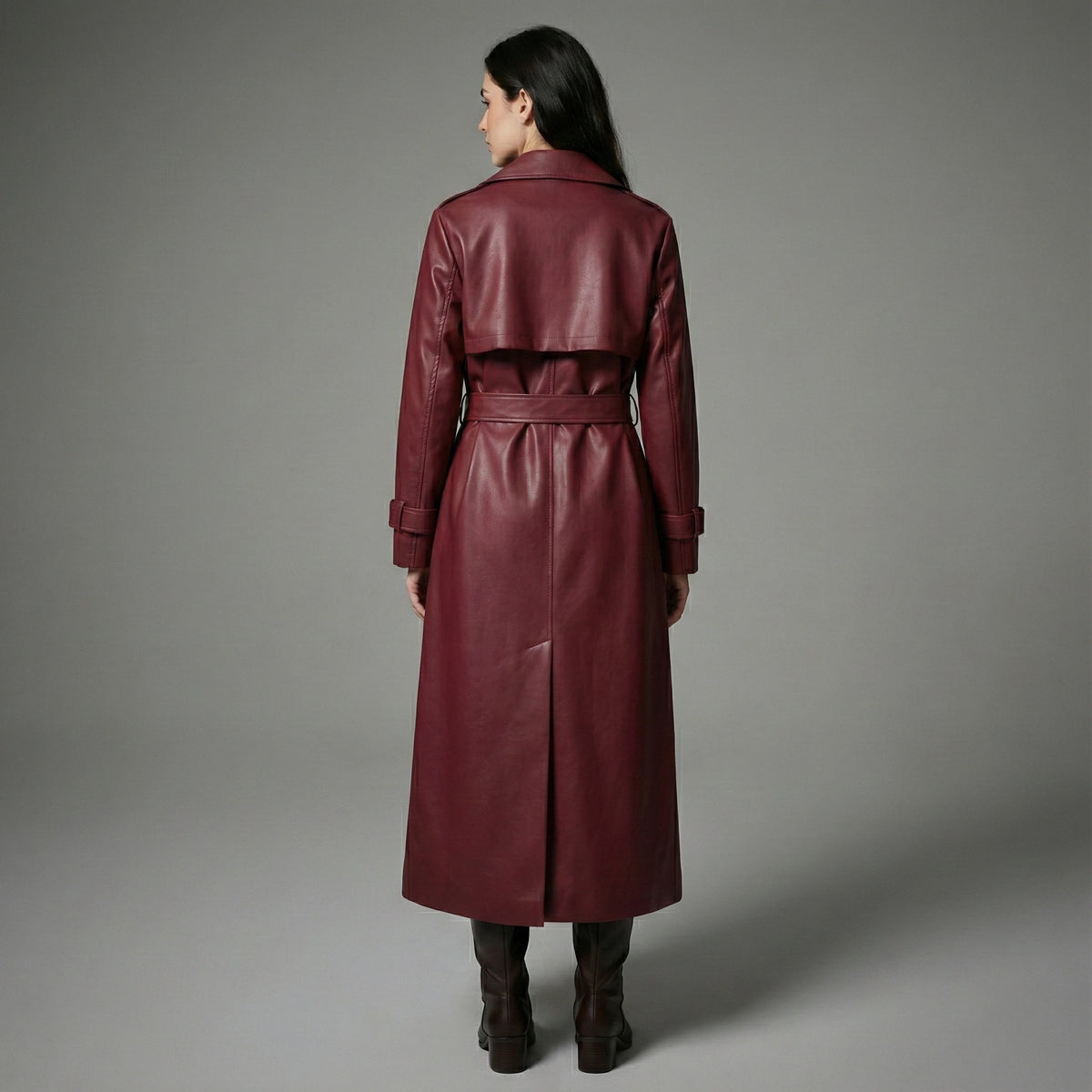 Woman wearing a burgundy leather trench coat against a gray background