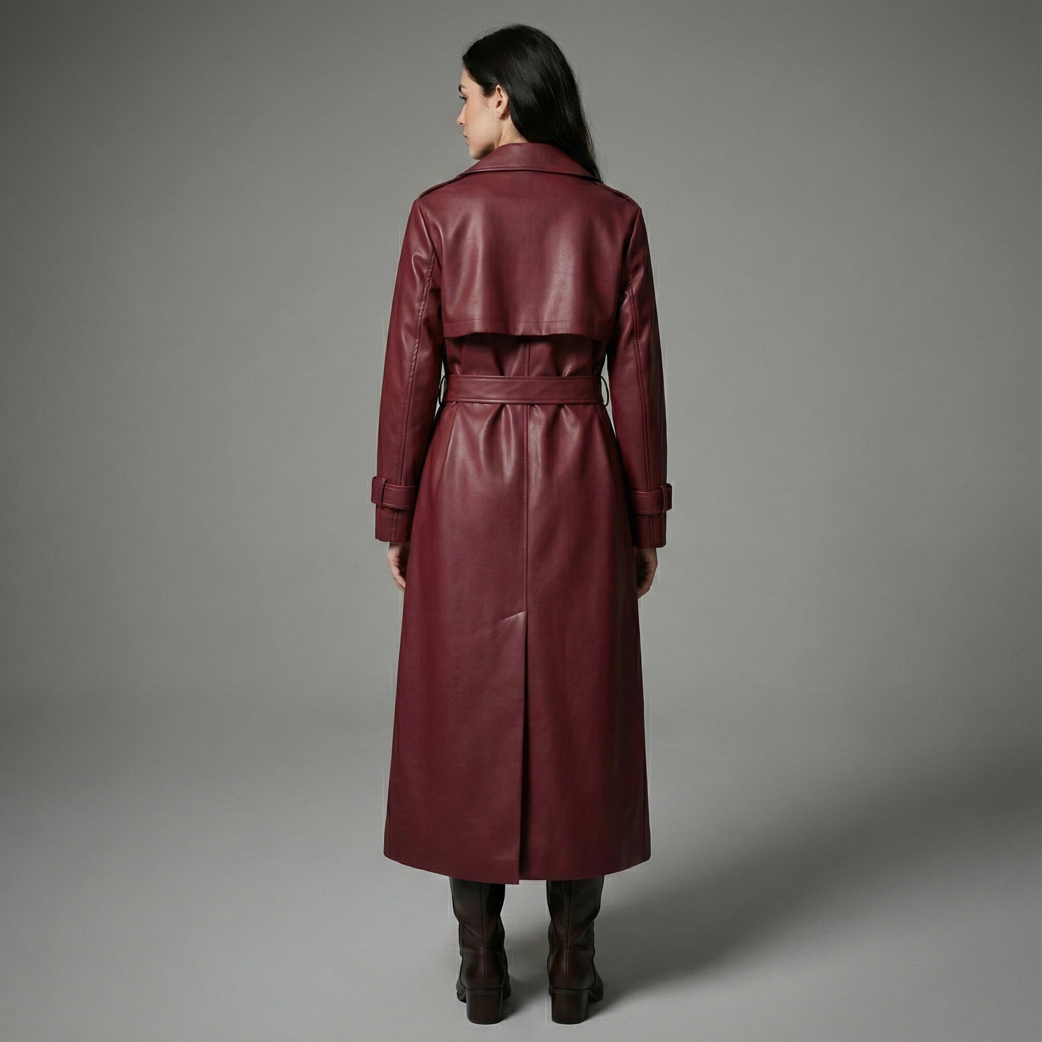 Woman wearing a burgundy leather trench coat against a gray background