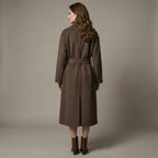 Woman wearing a brown coat standing against a plain background