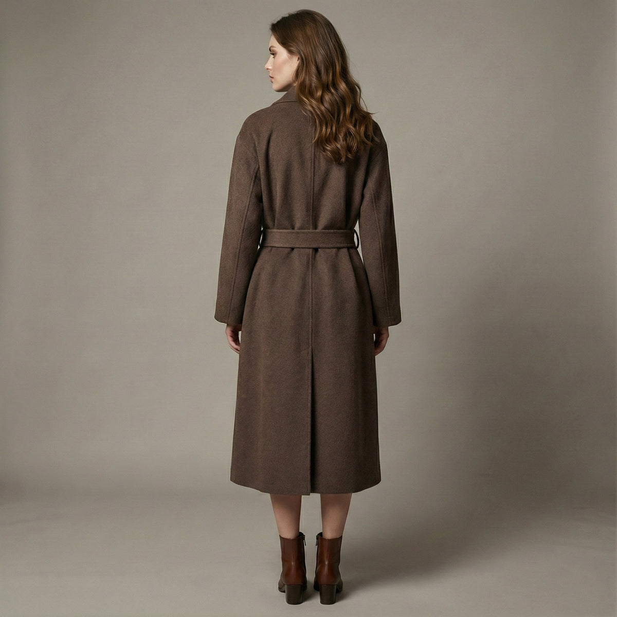Woman wearing a brown coat standing against a plain background