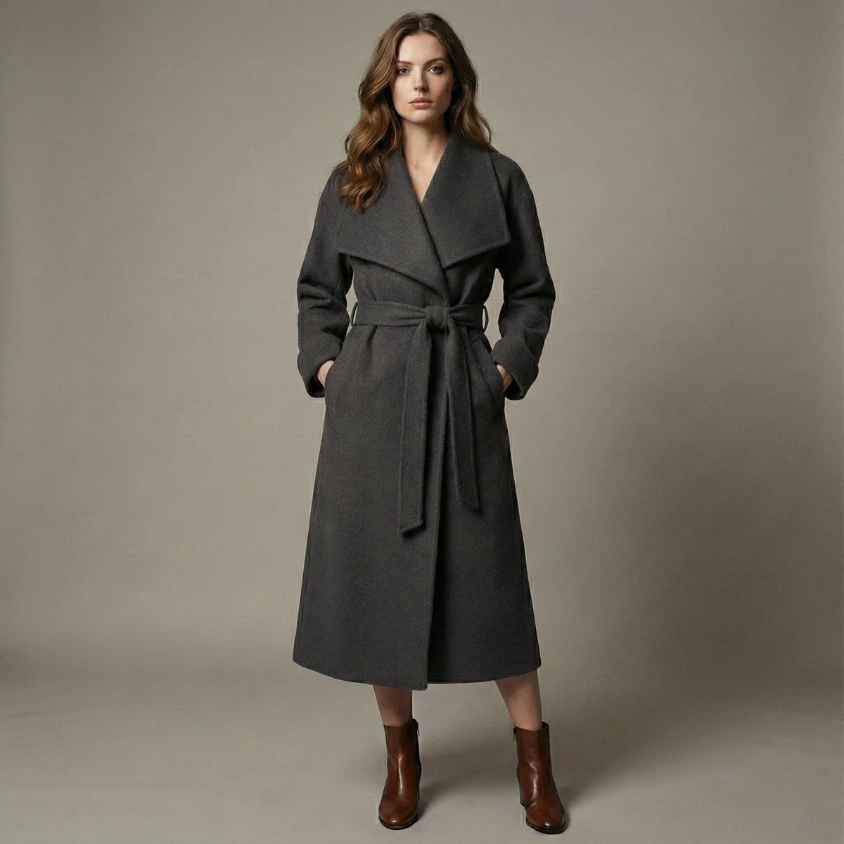 Woman wearing a gray coat with a belt against a plain background