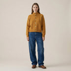 Woman wearing a mustard yellow sweater and blue jeans on a beige background