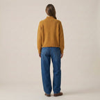 Person wearing a mustard yellow sweater and blue jeans on a beige background