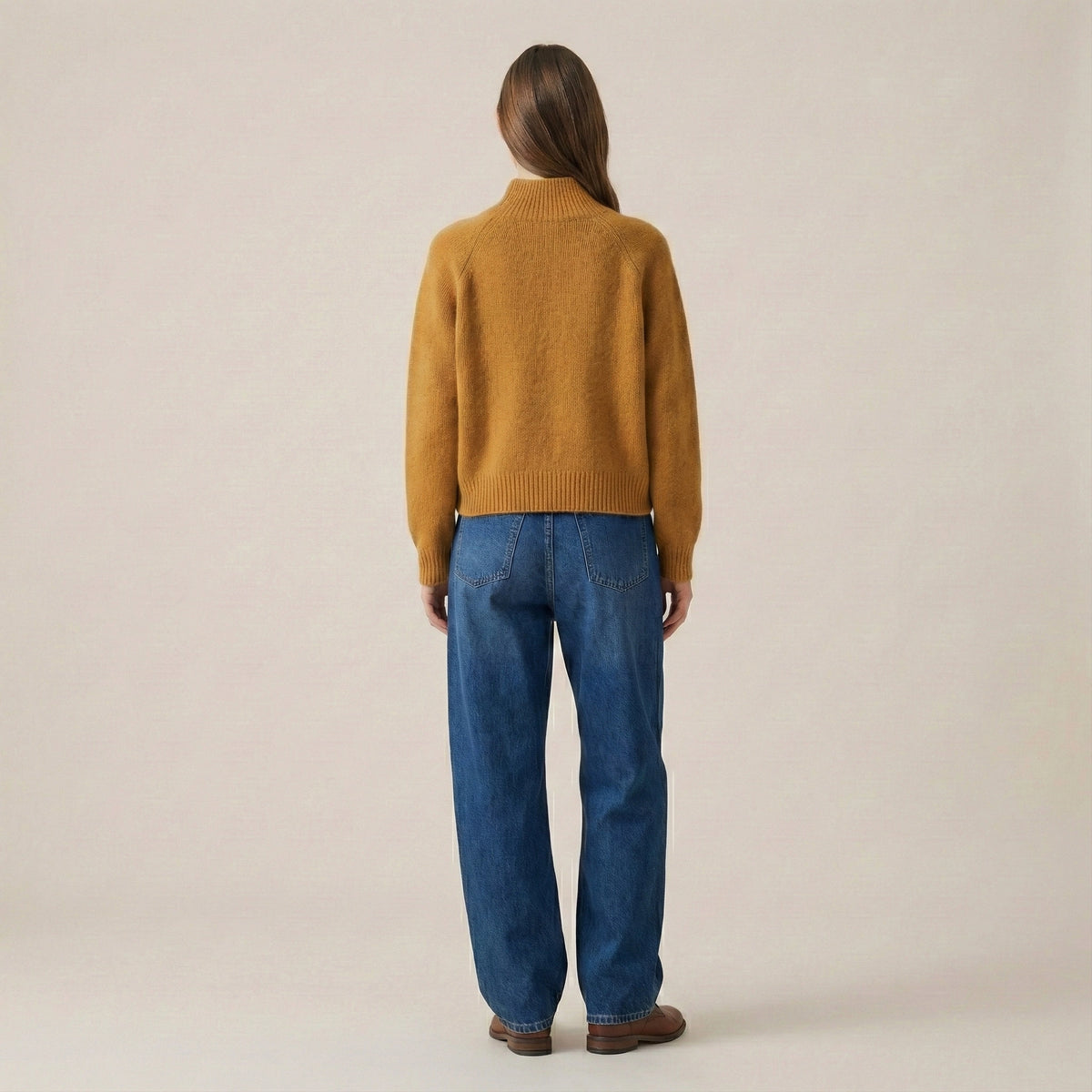 Person wearing a mustard yellow sweater and blue jeans on a beige background
