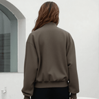 Person wearing a brown jacket standing in front of a white wall.