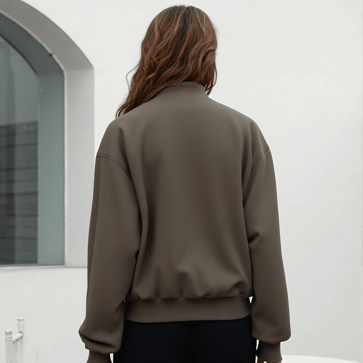 Person wearing a brown jacket standing in front of a white wall.