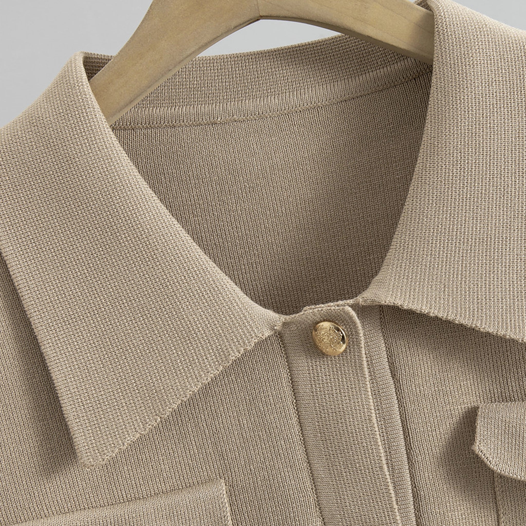 Close-up of a beige textured shirt with a button on a hanger