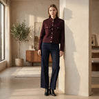 Woman wearing a burgundy jacket and dark blue jeans standing in a modern room.