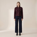 Woman wearing a burgundy jacket and dark jeans on a beige background
