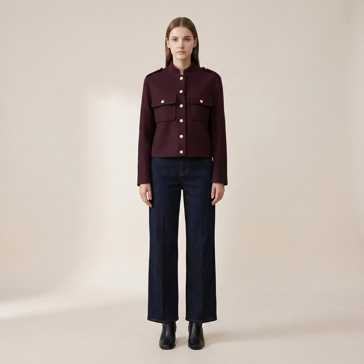 Woman wearing a burgundy jacket and dark jeans on a beige background