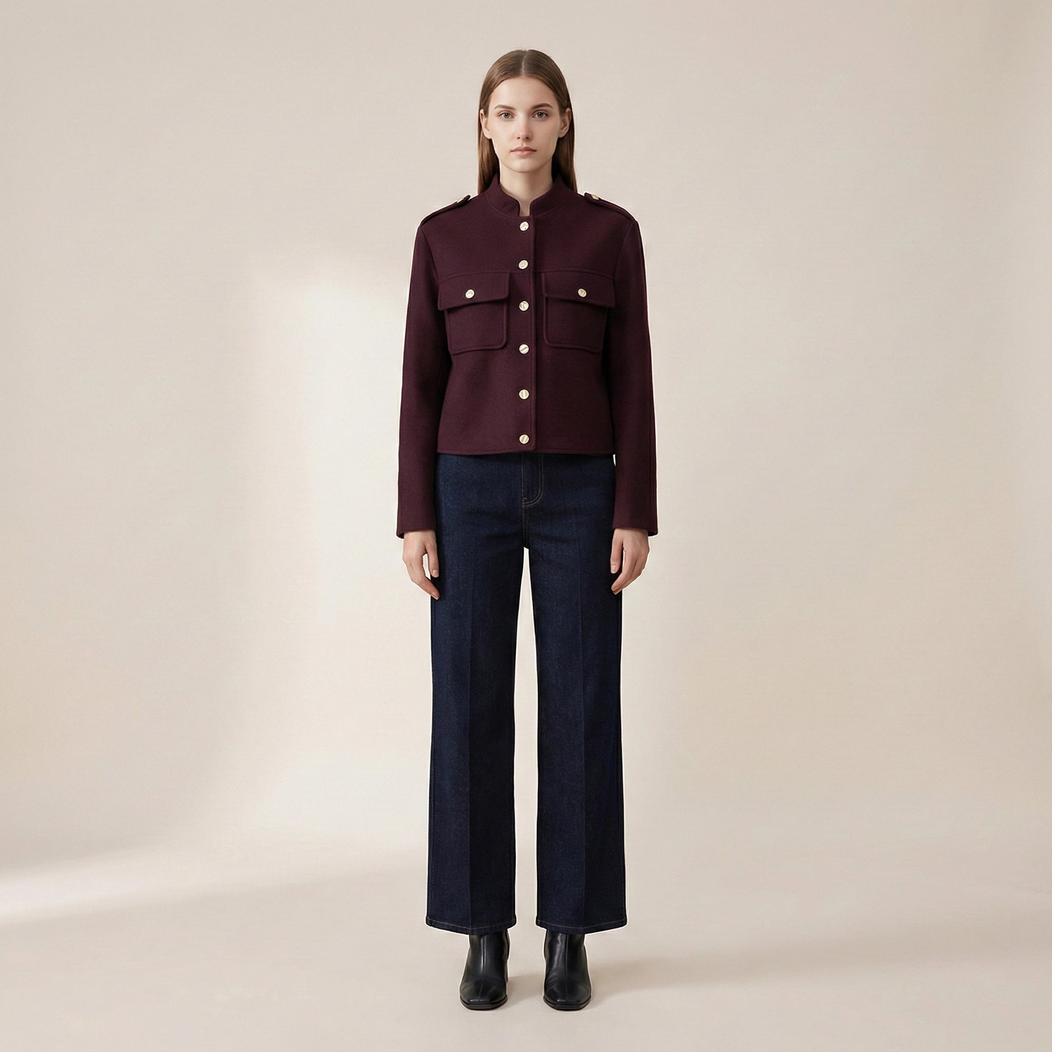 Woman wearing a burgundy jacket and dark jeans on a beige background