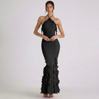 Woman wearing a black halter neck dress with ruffled details on a white background