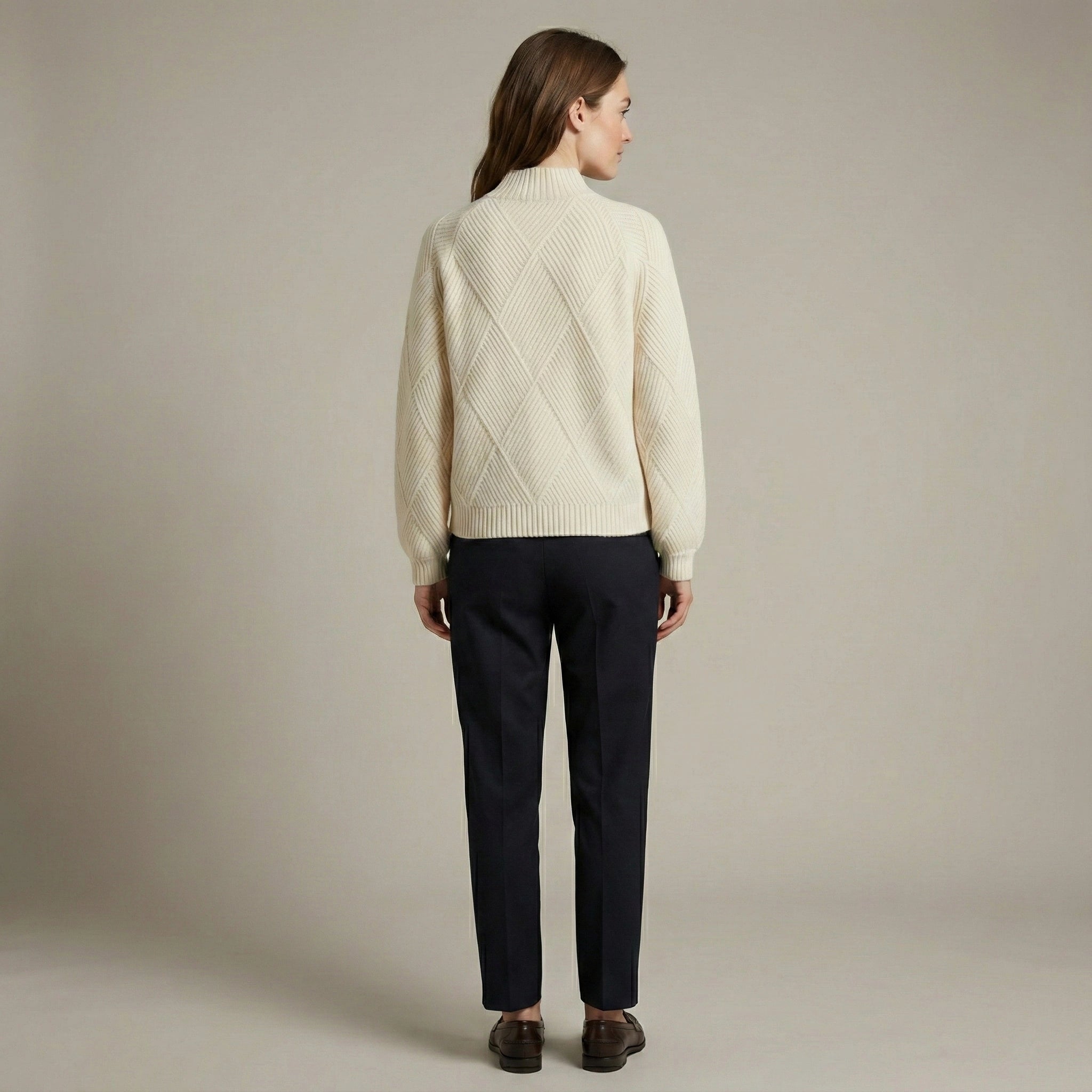 Woman wearing a cream sweater and dark pants against a plain background