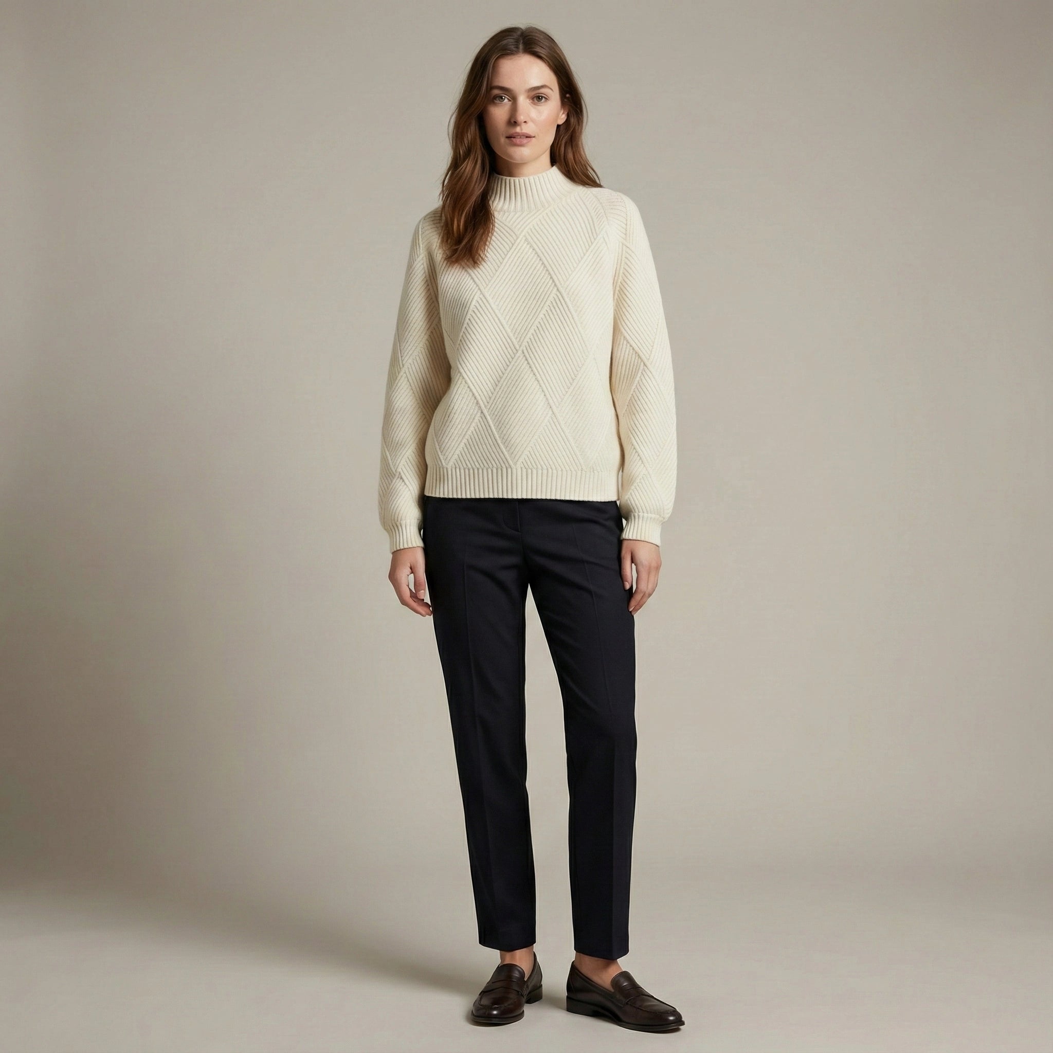 Woman wearing a cream sweater and black pants against a plain background